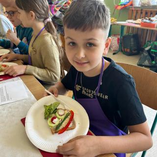 Uczeń z kolorową kanapką na talerzu.