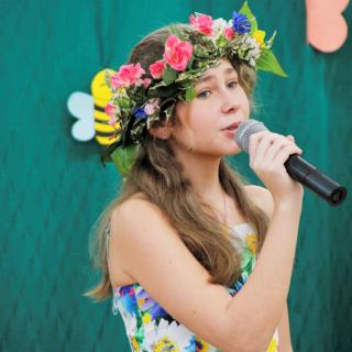 Dziewczynka w kolorowym wianku tzrymajacv mikrofon śpiewa piosenke "Wspomnienia są blisko"