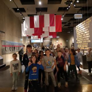 Uczniowie w muzeum, w tle biało-czerwone flagi.