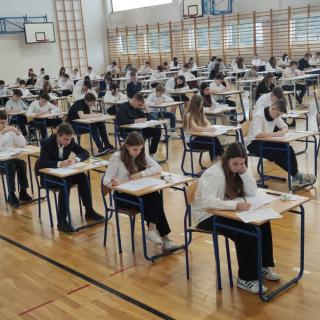 Uczniowie piszący egzamin na sali gimnastycznej.