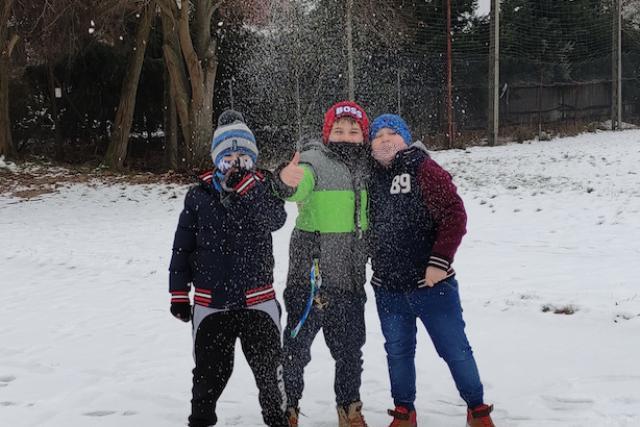 Grupa dzieci bawiąca się na zaśnieżonym boisku szkolnym