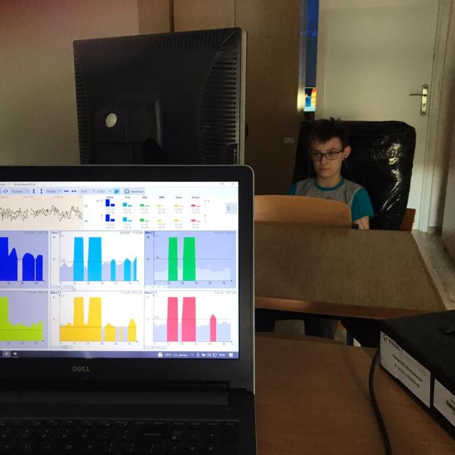 Z przodu ekran laptopa z wykresami, z tyłu siedzi uczeń wpatrzony w monitor.