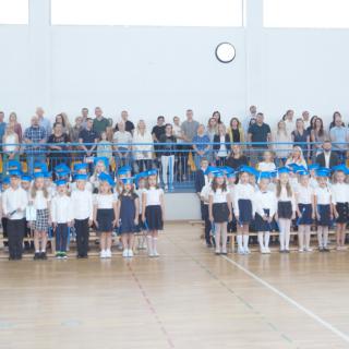 Uczniowie klas pierwszych stojący w sali gimnastycznej.