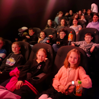 Ucznioiwe klasy piątej siedzą w sali kinowej.